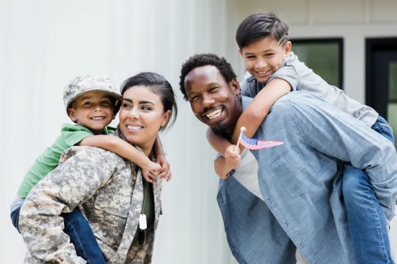 a veteran and her husband each holding one of their children on their back