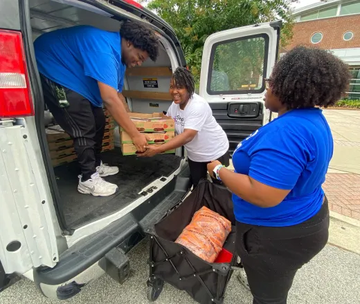 3 people bringing food off of a van